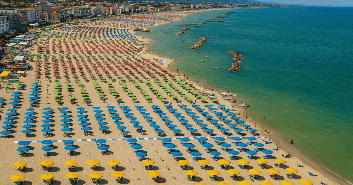 Vista aerea di uno stabilimento balneare con file di ombrelloni colorati lungo la costa, usata per l’articolo sulle gare delle concessioni balneari e sull’obbligo di avviarle anche senza il decreto indennizzi.
